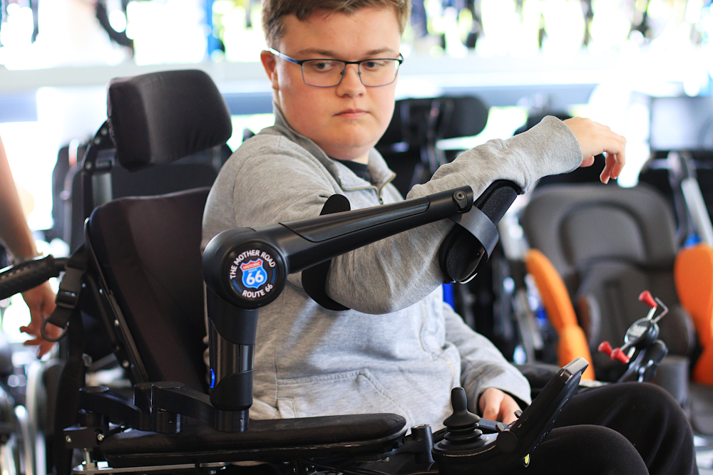 A user in their electric wheelchair with their robotic arm, the ORTHOPUS Supporter, customized.