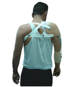 Photo d'un homme brun, vue de dos qui porte une prothèse mécanique blanche en haut du corps (elle basse au dessus et en dessous des épaules). L'homme porte un débardeur blanc et un pantalon noir. 