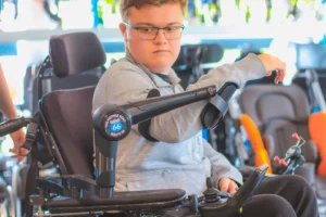 Young man using a power wheelchair equipped with a robotic assistive arm.